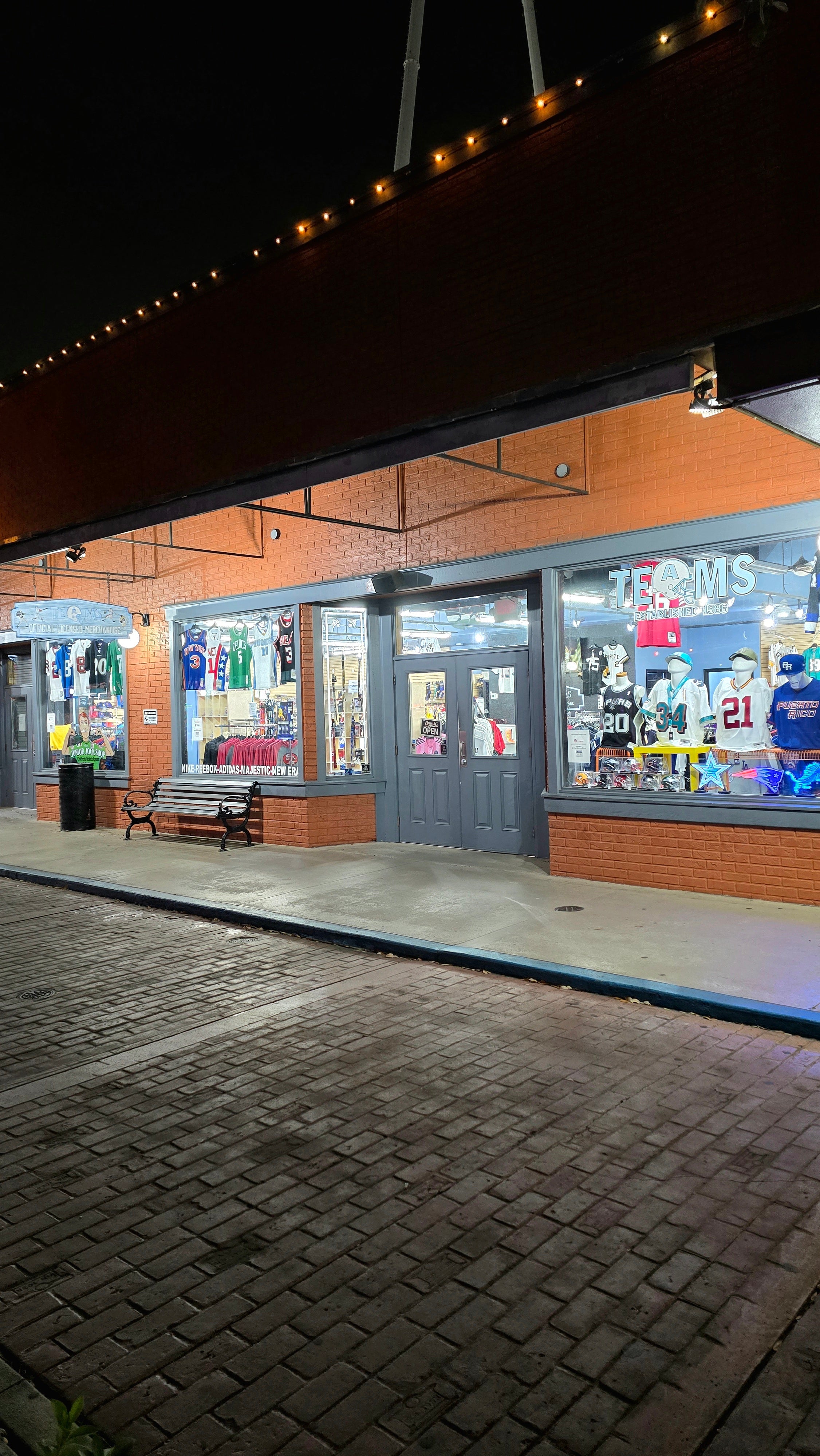 Storefront with glass windows displaying various items on a brick sidewalk at night.